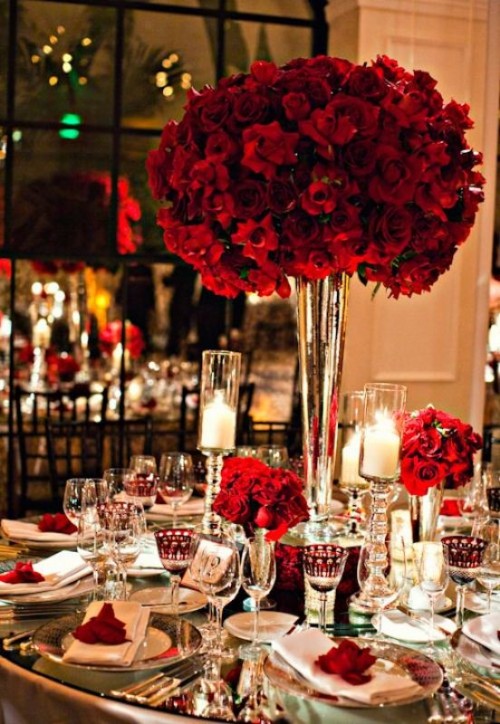 a lovely red rose wedding centerpiece of several lush arrangements and with red roses to mark each place setting is a beautiful idea