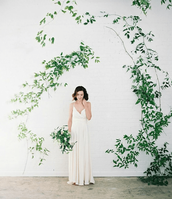 A wedding backdrop   a white brick wall and greenery branches attached in a whimsy way