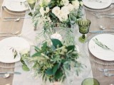 a beautiful neutral wedding tablescape with green glasses and chic greenery and white bloom centerpieces