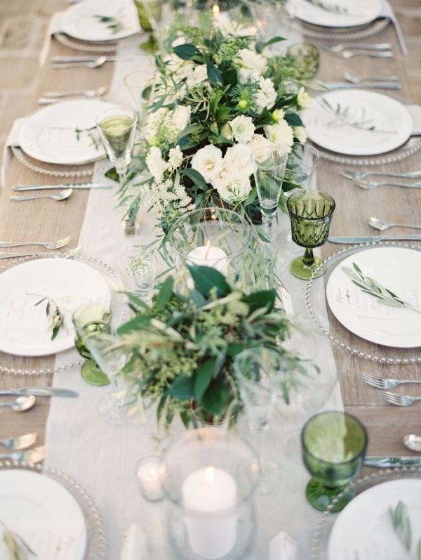 A beautiful neutral wedding tablescape with green glasses and chic greenery and white bloom centerpieces