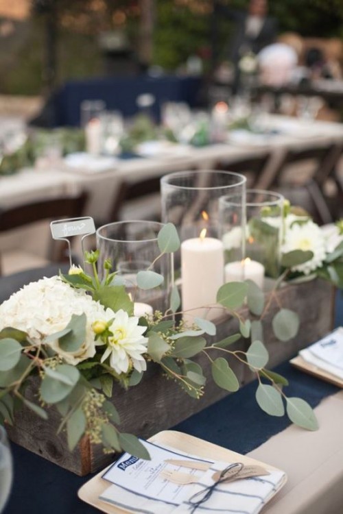 a simple wedding centerpiece of a wooden box, greenery and white blooms and candles