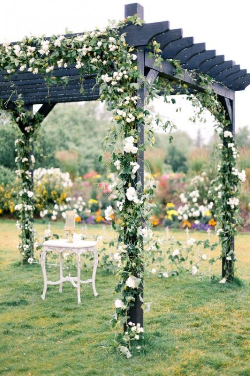 an organic wedding arch decorated with greenery and white blooms is a cool rustic idea to try