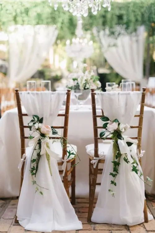 chairs decorated with white fabric, greenery and neutral blooms look very chic and beautiful