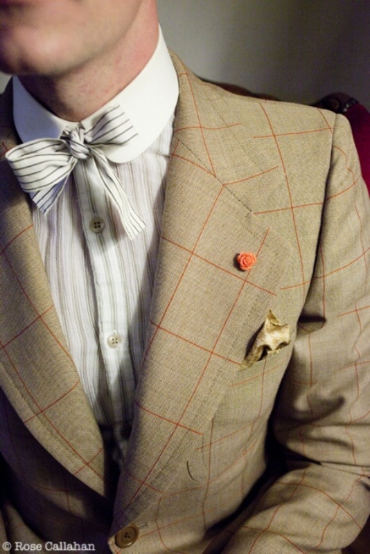 a vintage inspired groom's look with a tan chcked suit, a striped grey and white shirt with a bow and a tiny delicate boutonniere is pure elegance