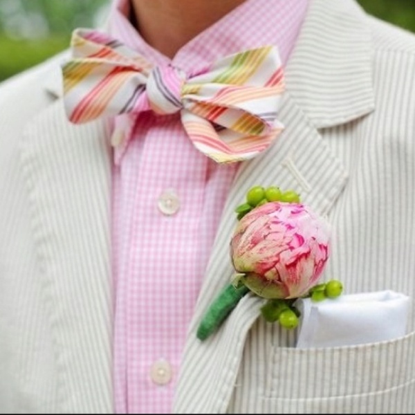 a bright groom's look with a pink checked shirt, a neutral striped blazer and a super bold printed bow tie plus a pink boutonniere