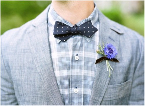 a grey suit, a grey and white checked shirt, a navy and white polka dot bow tie and a purple flower boutonniere for a slight touch of color