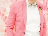 a bright groom’s outfit with a white shirt, a pink blazer, a bright checked bow tie and a bright striped belt is amazing
