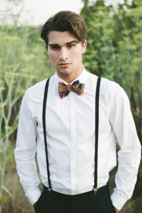 a bold groom's look with black pants, a white shirt, blakc thin supenders and a bold printed bow tie