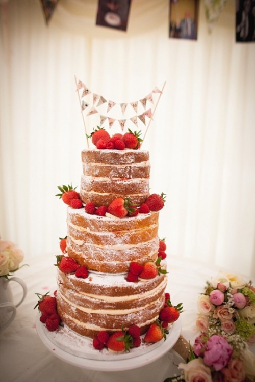 a naked wedding cake decorated with strawberries and topped with a bunting is a lovely idea for a summer wedding