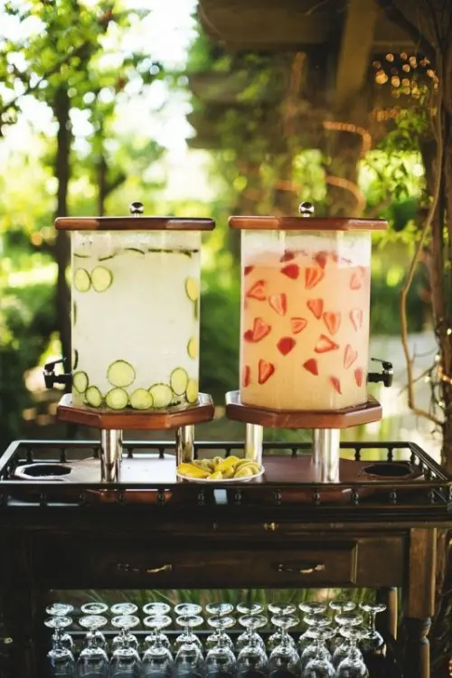 a drink station with cucumber and strawberry lemonade and glasses is a stylish and cool idea for a summer wedding
