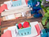 a stylish summer wedding tablescape with delicate blooms and greenery, woven placemats and porcelain, coral nappkins and blue boxes with fresh berries as wedding favors