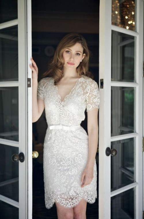 a very delicate white lace mini dress, semi-fitting, with short sleeves a V-neckline, buttons on the bodice and a bow on the waistline