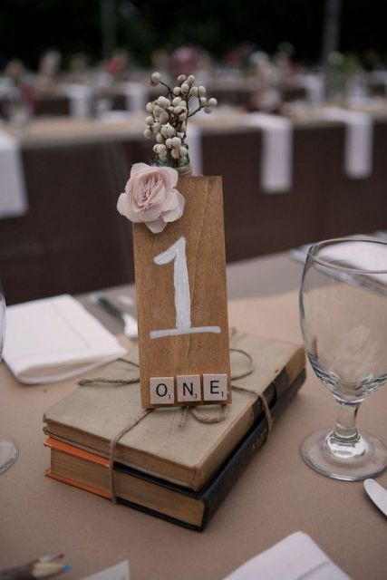 vintage books with a tie, a plywood table number and a pink bloom for a book lover wedding