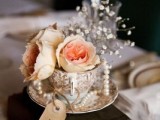 a stack of vintage books, a vintage teacup with fresh blooms, pearls, baby’s breath and a tag for a vintage wedding