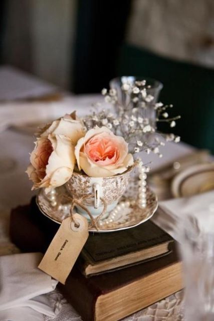 a stack of vintage books, a vintage teacup with fresh blooms, pearls, baby's breath and a tag for a vintage wedding