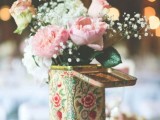 a stack of books with a tin can and a pink floral arrangement will fit a boho or a rustic wedding