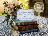 a vintage book wedding centerpiece with a quote, a candle in a glass and some blooms behind