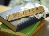 a stack fo vintage books with scrabble letters, a doily and some baby’s breath in a bottle