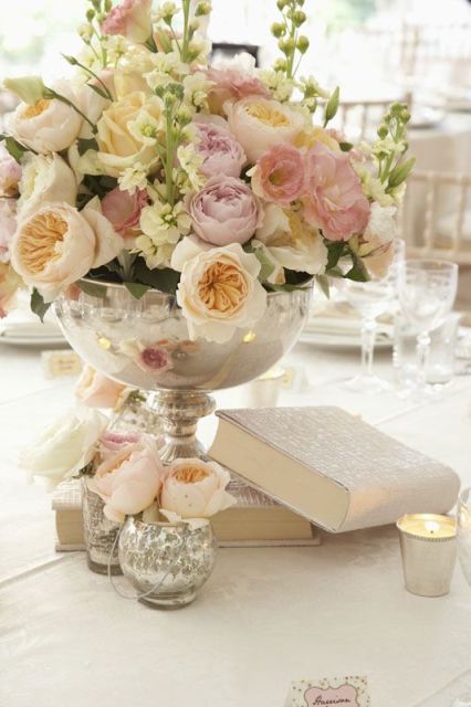 some books and a large bowl with a lush blush and iivory florla arrangement for a vintage-inspired wedding