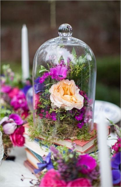 a stack of books with a cloche filled with moss and bright blooms is a gorgeous idea of wedding decor