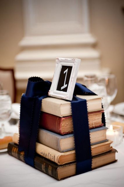 a stack of vintage books with navy ribbon to match the wedding color scheme and a table number on top