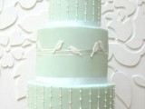 a cute pastel green wedding cake decorated with white beads and birds on its sides for a spring wedding