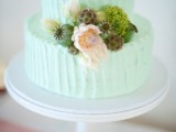 a casual textural buttercream mint green wedding cake with blooms, greenery and moss