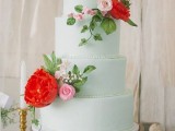 an elegant mint green wedding cake with pink and red fresh flowers and a monogram on top