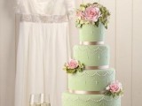 a mint green wedding cake decorated with shiny ribbons, edible beads and pink sugar flowers on various tiers