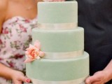 a matte mint green wedding cake with shiny ribbon and fresh pink blooms on it