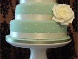 a cute mint green wedding cake with shiny ribbon, beads and a single white bloom on its side