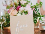 a large kraft paper table number with calligraphy and on a chic and refined stand to elevate its look