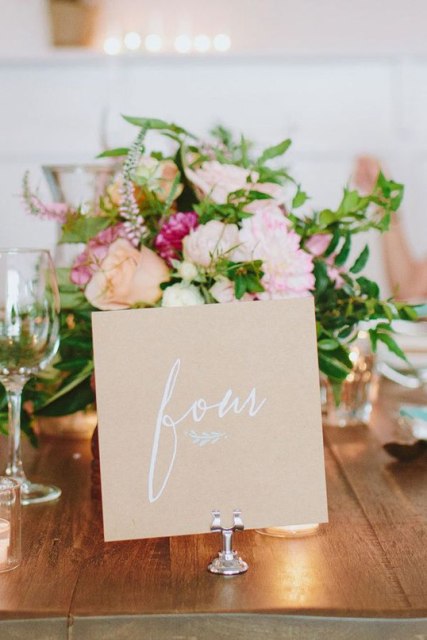 a large kraft paper table number with calligraphy and on a chic and refined stand to elevate its look