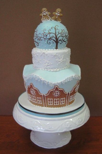 a beautiful blue and white winter wedding cake with a ball on top decorated with gingerbread cookies - house-shaped ones and people-shaped ones on top