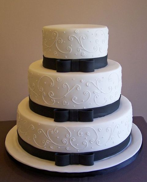 a white patterned wedding cake with black ribbons and black bows for a contrasting and bold look, for a chic and lovely wedding with a vintage feel
