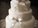 a white wedding cake with plain and patterned tiers, with white ribbon bows and embellished brooches is a chic and refined idea for a wedding with a vintage feel