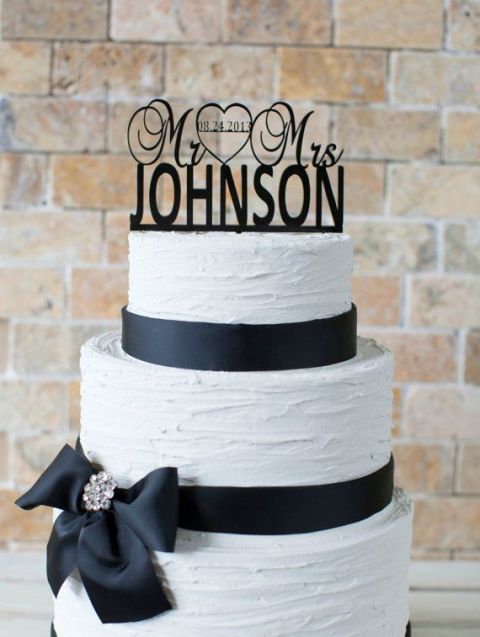 a white textural wedding cake with black ribbons and a black bow, an embellished brooch, a black silhouette cake topper is a stylish idea for a black and white wedding