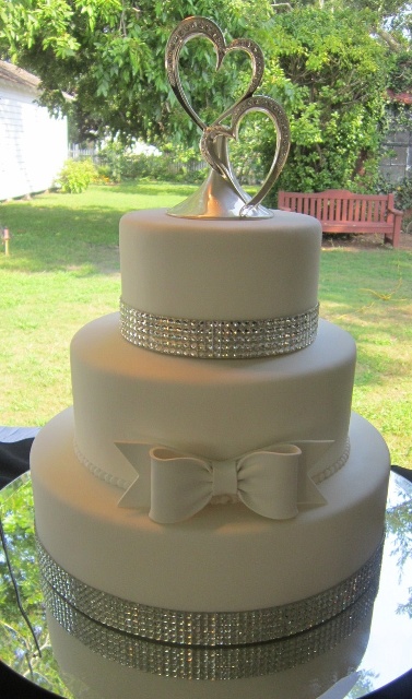 a white wedding cake with embellishments, a white sugar bow and embellished hearts on top is a chic and stylish idea for a glam wedding