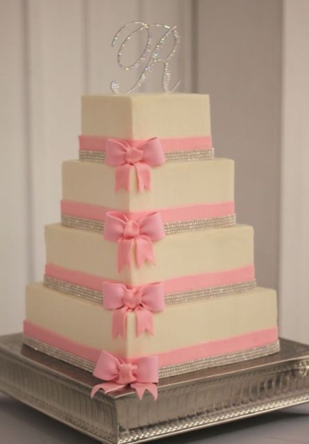 a square wedding cake with pink sugar bows and embellishments, an embellished monogram is a pretty solution for a modern wedding with a glam feel