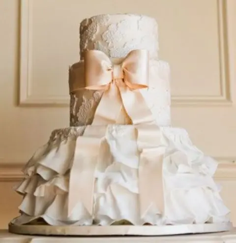 a nude lace and ruffle wedding cake with a beige sugar bow is a lovely idea for a vintage-inspired wedding done in neutrals