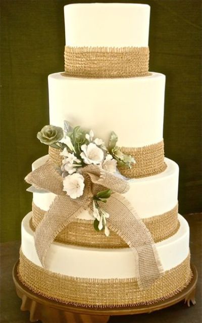a white buttercream wedding cake decorated with burlap ribbons and a burlap bow, with blooms is a perfect rustic wedding cake