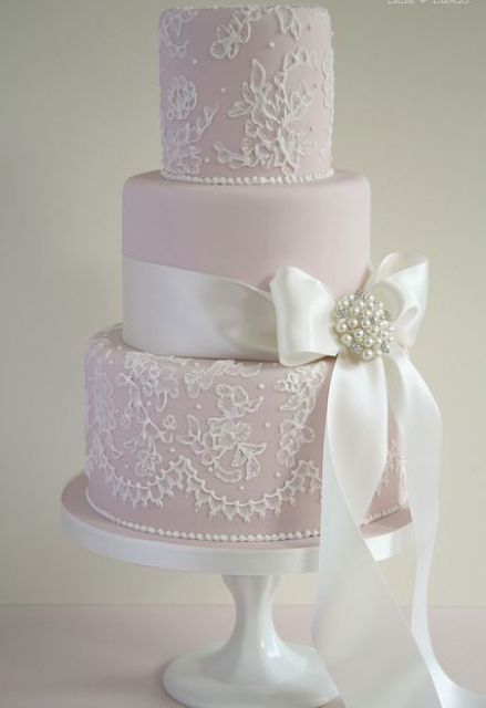 an elegant and refined light pink wedding cake with lace detailing and a white silk ribbon with an embellished brooch is a lovely and cool idea