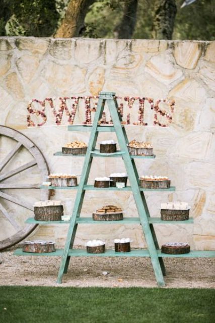 a rustic wedding dessert bar of a blue ladder, some wood slices with desserts and a wine cork word on the wall