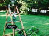 a rustic wedding decoration of a ladder, a chalkboard sign and some greenery and blooms