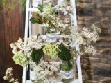 a rustic wedding decoration of a white ladder and lots of simple blooms and wildflowers in jars