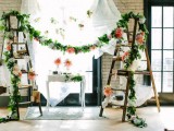 a bright summer wedding decoration of ladders, greenery and floral garlands, books and candles and an airy white curtain