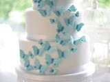 a white wedding cake decorated with a bunch of blue butterflies is a lovely and chic idea of a wedding dessert to rock