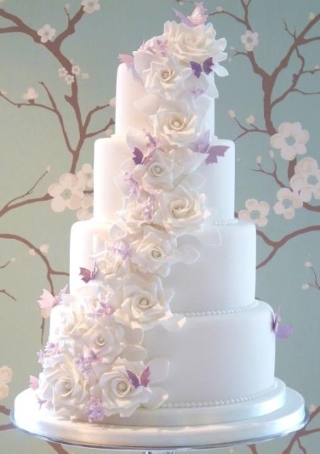 a white wedding cake decorated with white sugar blooms and lilac butterflies is a lovely and very sweet idea for your wedding