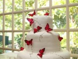a white wedding cake decorated with red butterflies and their paths painted on the cake is a non-traditional and cool wedding dessert idea