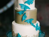 a white and gold wedding cake decorated with blue butterflies and gold floral patterns painted on the piece is a bright and chic idea